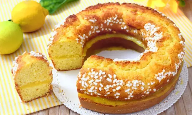 Un soffice ciambellone al limone, decorato con perline di zucchero, con una fetta tagliata che rivela un ripieno cremoso.