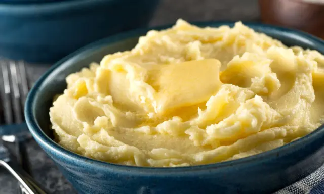 Una ciotola blu piena di soffice purea di patate, con una fetta di burro che si scioglie sopra.