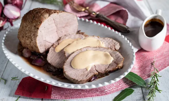 Arrosto di vitello morbido con sughetto benedetta, servito su un piatto bianco con cipolle rosse caramellate e rosmarino.