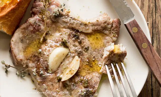 Braciola di maiale succulenta, condita con aglio e erbe aromatiche, servita con pane croccante.