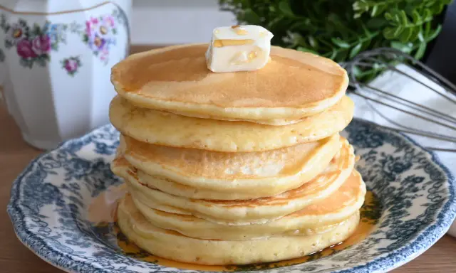 Pila di soffici pancake con farina di avena, guarniti con burro e sciroppo d'acero, su un piatto decorato.