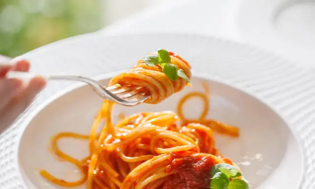 Un primo piatto invitante: spaghetti al dente conditi con un sugo rosso vivo di pomodorini freschi e basilico, pronti per essere gustati.