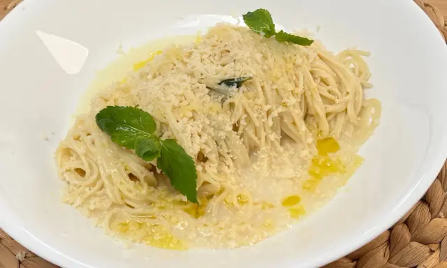Spaghetti al limone cremosi, cosparsi di parmigiano e guarniti con foglie di menta fresca.