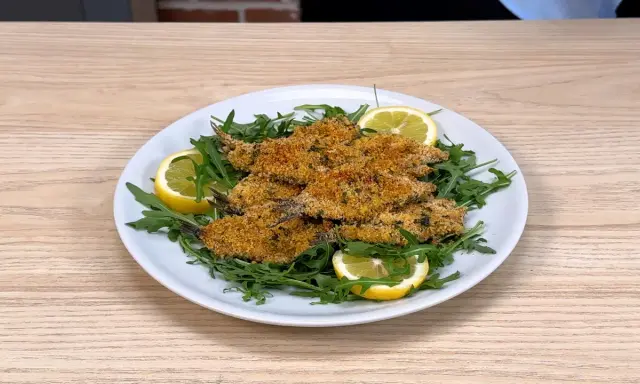 Piatto di alici al forno dorate e croccanti, servite su un letto di rucola fresca con spicchi di limone.