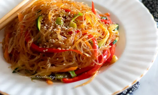 Deliziosi spaghetti di soia con verdure colorate, peperoni rossi, zucchine e carote, guarniti con semi di sesamo.