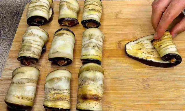 Involtini di melanzane pronti per essere infornati. Una mano sta arrotolando l'ultima fetta di melanzana grigliata.