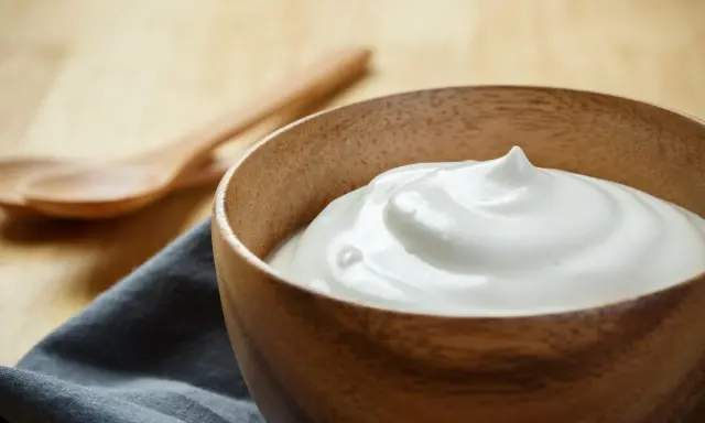 Una ciotola di legno piena di soffice crema al latte, pronta per essere gustata con due cucchiai in legno sullo sfondo.
