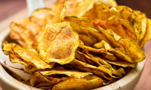 Croccanti chips di zucchine dorate, perfette per uno snack sano e gustoso, servite in una ciotola di legno.