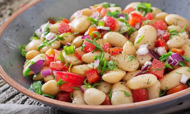 Insalata di fagioli bianchi, pomodori, cipolla rossa e erbe fresche in una ciotola rustica. Un piatto leggero e saporito.