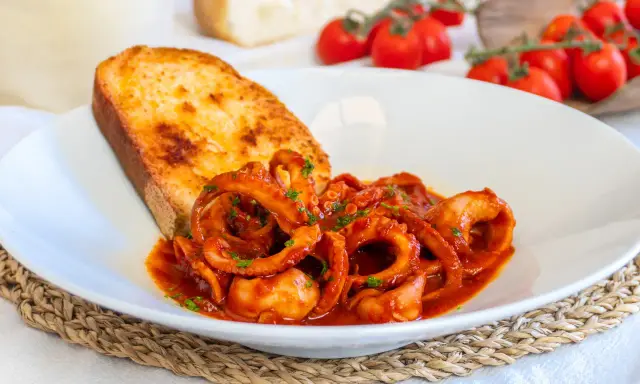 Moscardini in umido, teneri e saporiti, serviti con pane tostato e pomodorini freschi.