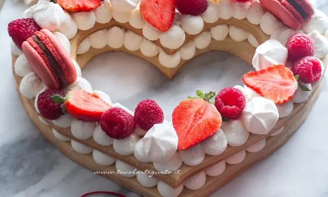 Deliziosa cream tart a forma di cuore per bambini, decorata con fragole, lamponi, meringhe e macarons.