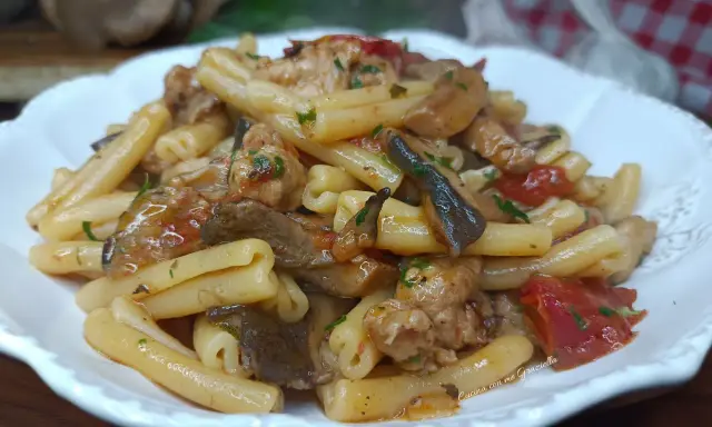 Un piatto invitante di pasta funghi e salsiccia, condita con pomodoro e prezzemolo, pronta per essere gustata.