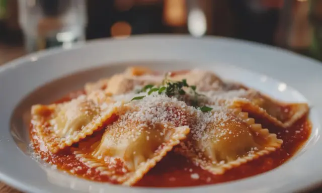 Deliziosi ravioli fatti in casa, conditi con sugo rosso, parmigiano grattugiato e un rametto di erbe aromatiche.