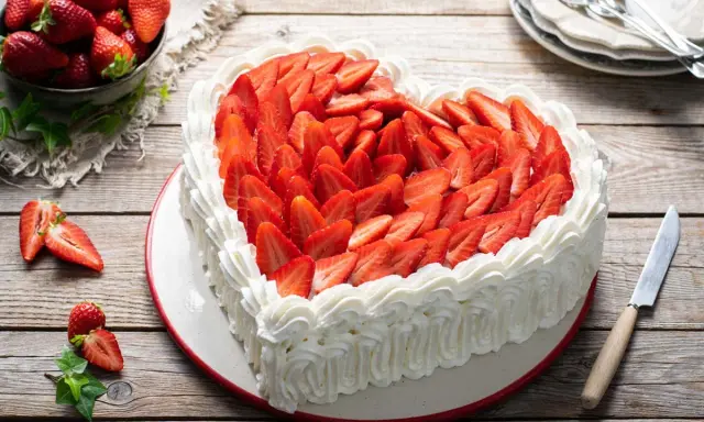 Cuore di torta panna e fragole, decorato con panna montata e fragole fresche a fette. Un invito alla dolcezza.