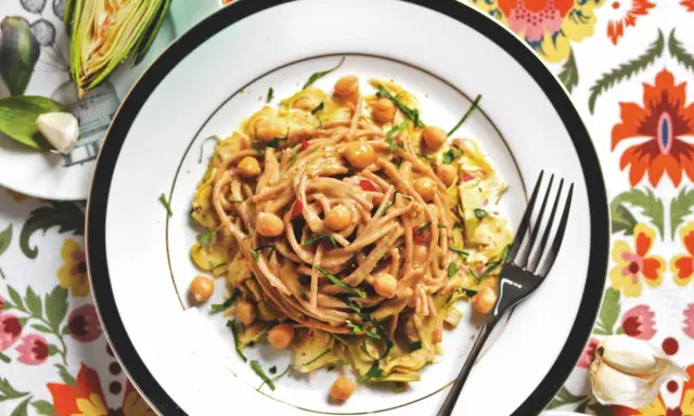 Un piatto invitante di pasta con carciofi alla siciliana, arricchito da ceci e erbe fresche, su un tovagliolo colorato.