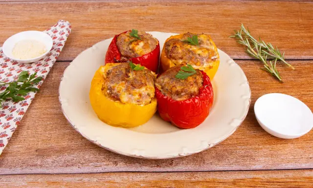Quattro peperoni ripieni al forno, rossi e gialli, con un ripieno saporito e dorato, guarniti con prezzemolo fresco.
