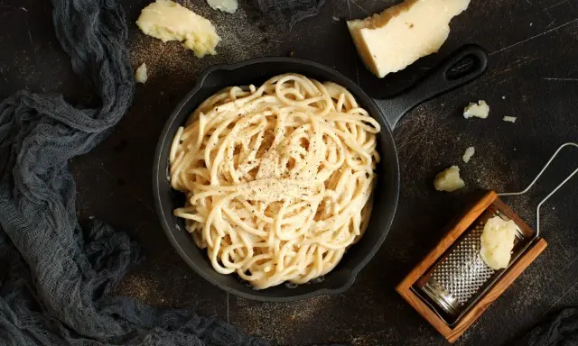 Un piatto di spaghetti cacio e pepe fumante, con pezzi di pecorino e una grattugia in legno.