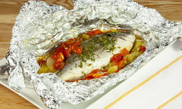 Orata al cartoccio con pomodorini e verdure, cotta al forno e servita in un foglio d'alluminio aperto.