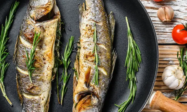 Due branzini dorati in padella, profumati al rosmarino, pronti per essere gustati.