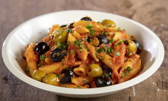 Penne al sugo rosso con olive nere e verdi, capperi e prezzemolo, un piatto di pasta alla puttanesca invitante.