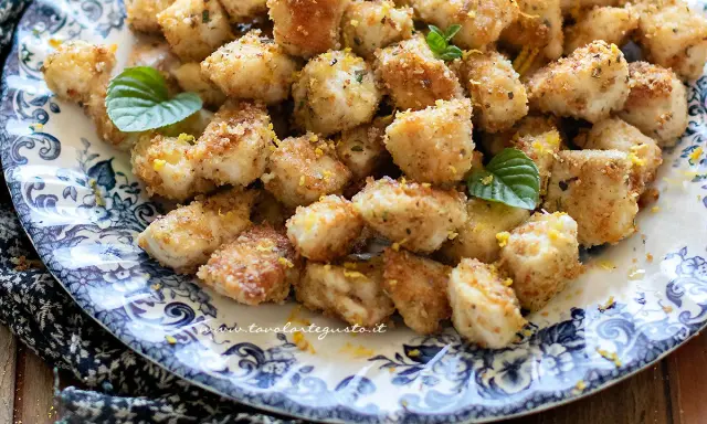 Bocconcini di pollo dorati e croccanti, guarniti con scorza di limone e foglie di menta fresca su un piatto decorato.