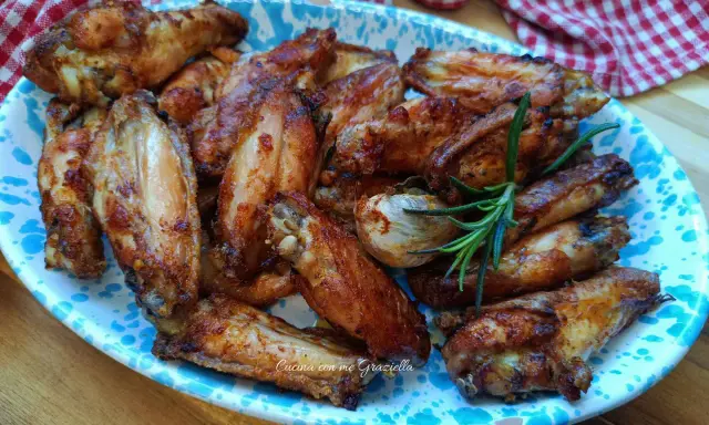 Alette di pollo dorate e croccanti, servite su un piatto decorato con un rametto di rosmarino.