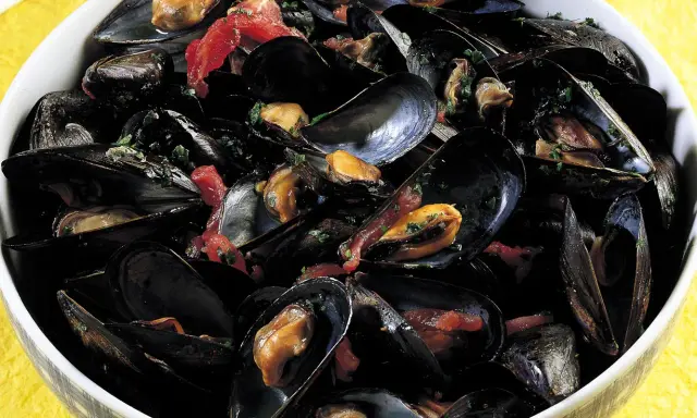 Una ciotola piena di saporita zuppa di cozze, con cozze nere aperte che rivelano la polpa succulenta, condita con erbe fresche e pomodoro.