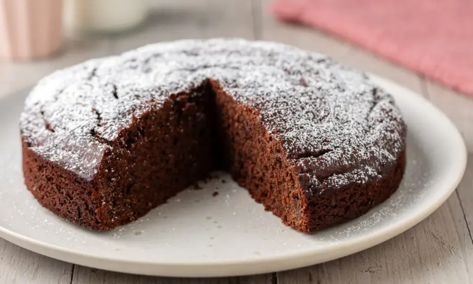 Una fetta è stata tolta da una torta al cioccolato morbida, cosparsa di zucchero a velo.