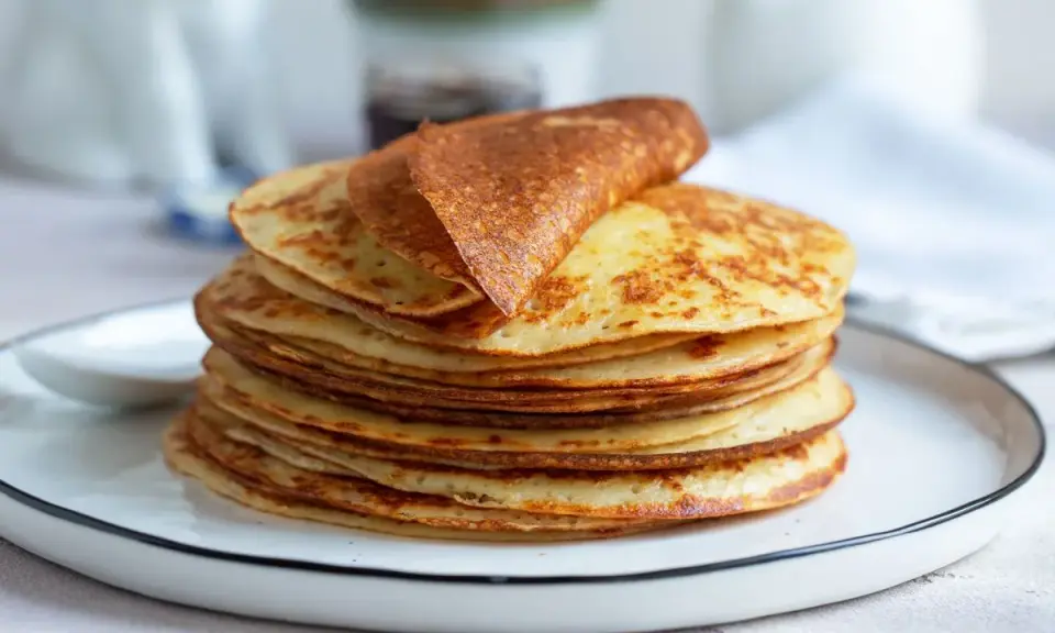 Una pila di dorate crepes senza glutine, una piegata in cima, su un piatto bianco.