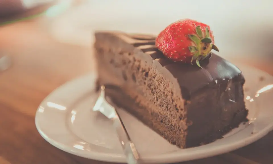 Una fetta di torta al cioccolato, ricoperta di glassa lucida e guarnita con una fragola fresca, pronta per essere gustata.