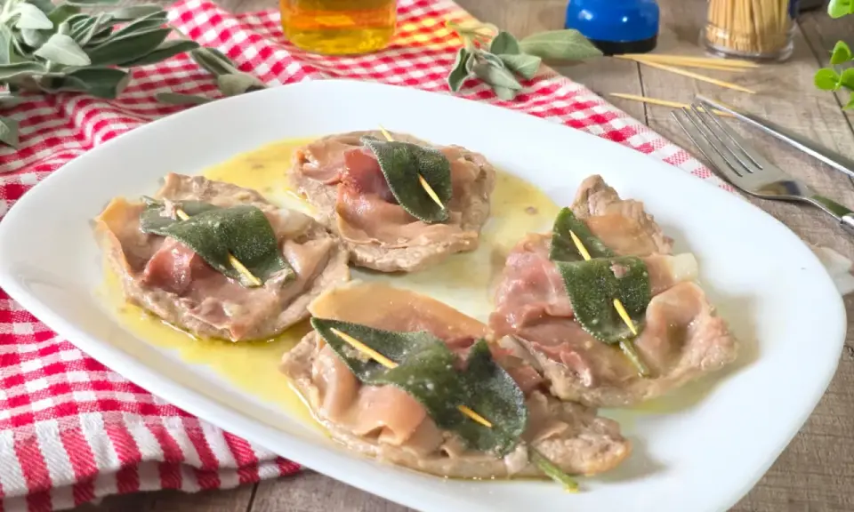 Saltimbocca alla romana su piatto bianco, con prosciutto crudo e salvia, su un tavolo di legno.