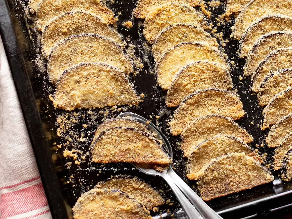 Fette di melanzane al forno, dorate e croccanti, disposte su una teglia. Un contorno saporito e leggero.