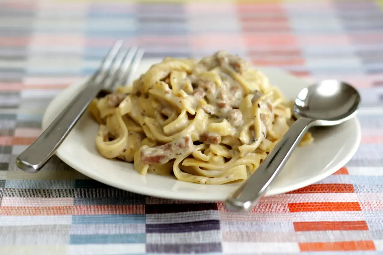 Un piatto di tagliatelle ai funghi cremose, con forchetta e cucchiaio pronti per gustare questo delizioso primo.