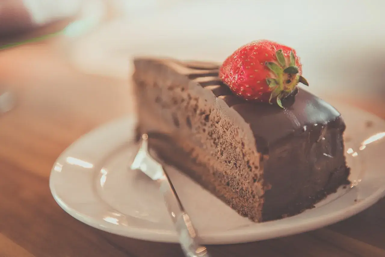 Una fetta di torta al cioccolato, ricoperta di glassa lucida e guarnita con una fragola fresca, pronta per essere gustata.