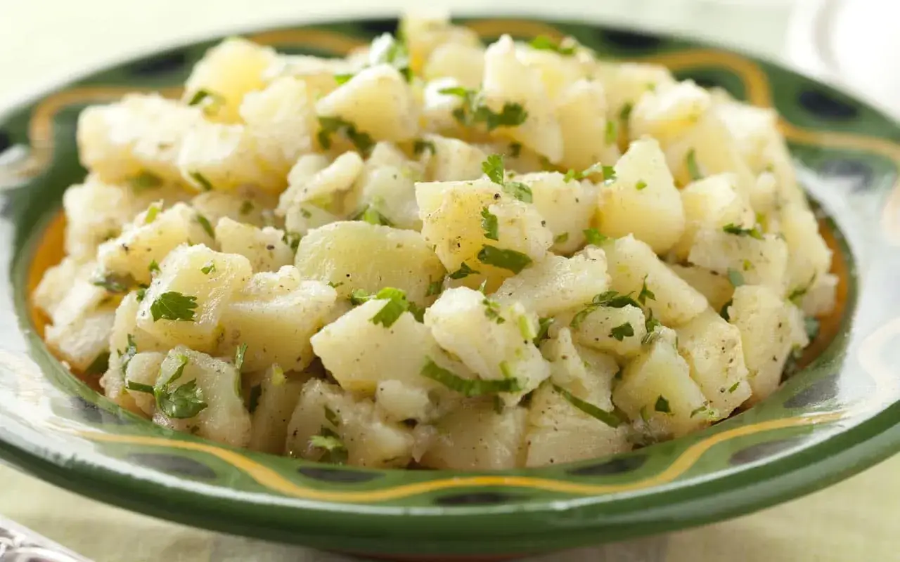 Un'insalata di patate fresca e saporita, condita con erbe aromatiche e servita in un piatto decorato.