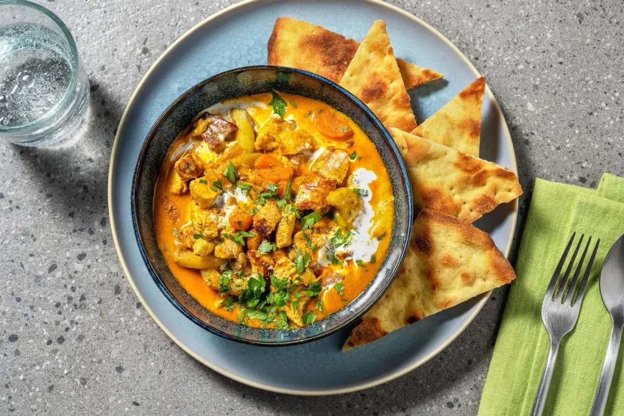 Un invitante pollo al curry cremoso, guarnito con coriandolo fresco e servito con pane naan croccante.