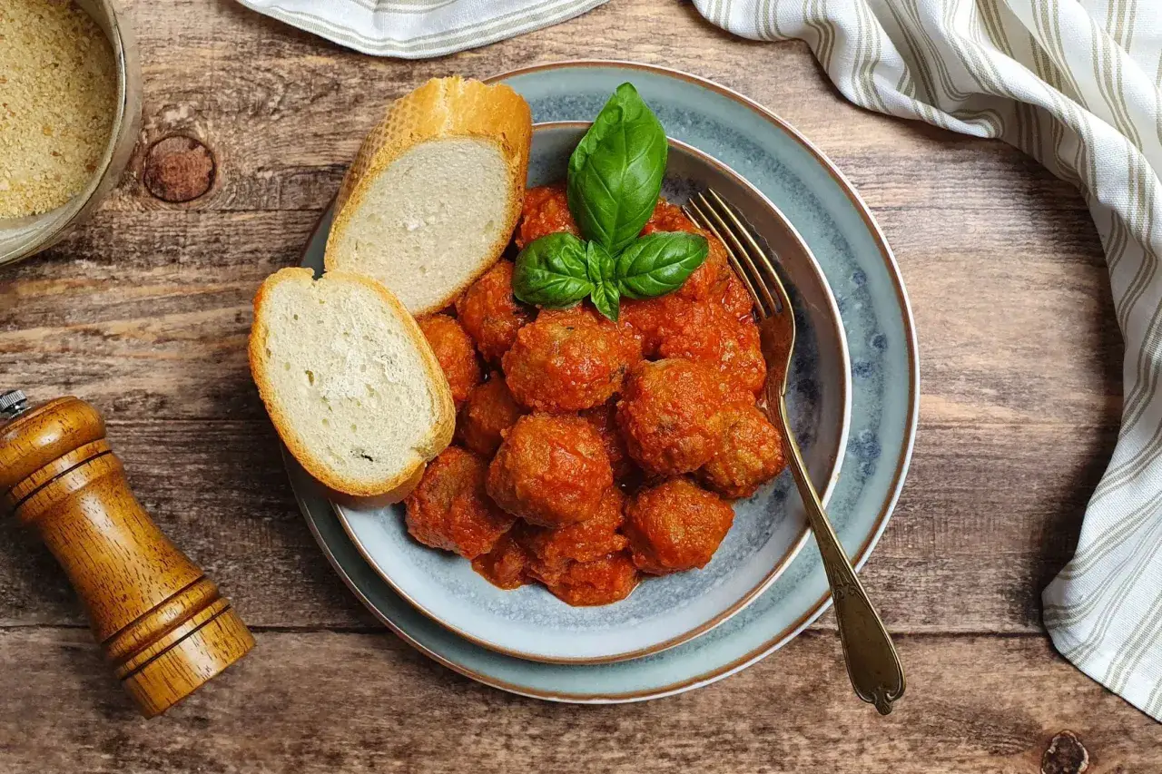 Succulente polpette al sugo, guarnite con basilico fresco, accompagnate da fette di pane croccante su un piatto blu.