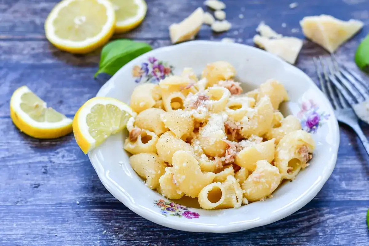Piatto di pasta al tonno in bianco, condita con parmigiano e guarnita con spicchi di limone fresco. Un classico saporito.