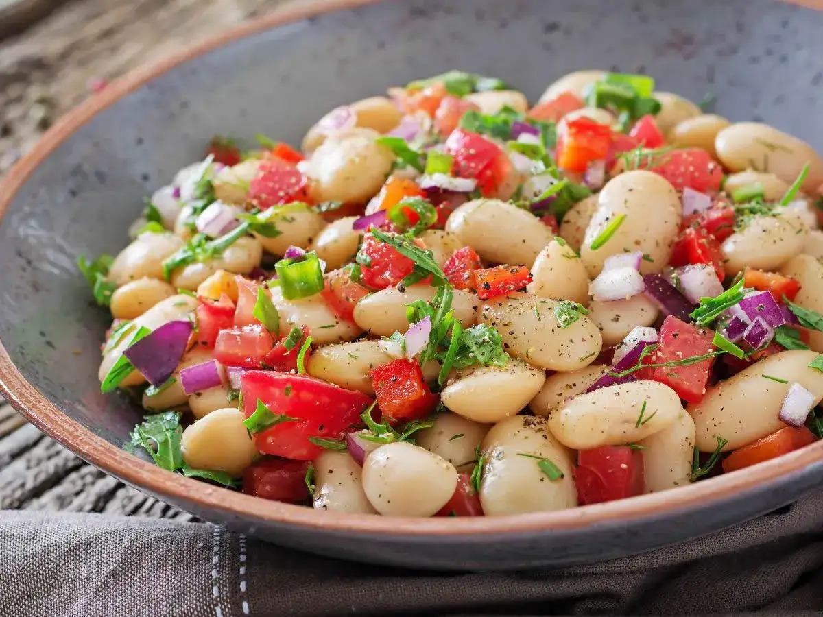 Insalata di fagioli bianchi, pomodori, cipolla rossa e erbe fresche in una ciotola rustica. Un piatto colorato e salutare.
