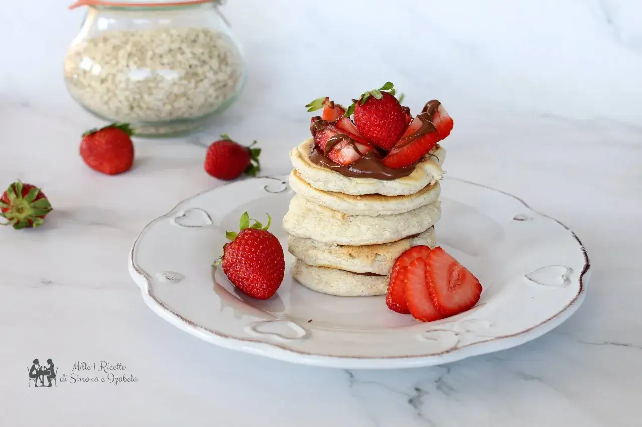 Pancake con farina di avena, guarniti con fragole fresche e crema al cioccolato, su un piatto bianco decorato.