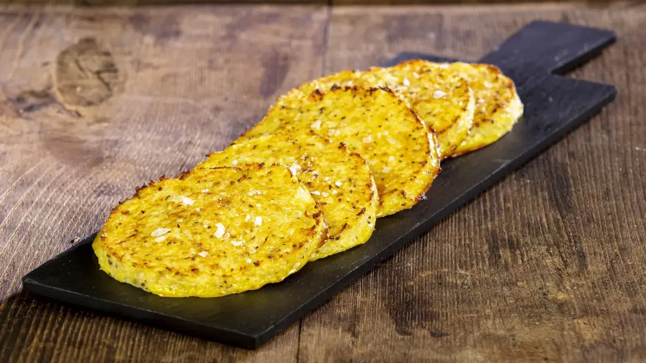 Fette dorate di cavolfiore al forno con pangrattato e formaggio, croccanti e saporite, servite su una lavagna nera.