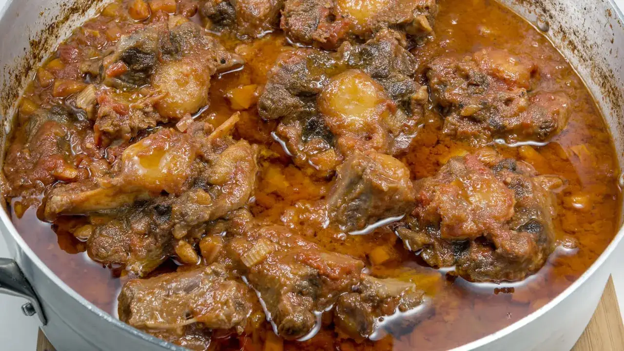 Un saporito coda alla vaccinara in umido, con pezzi di carne tenera e sugo rosso, pronto per essere gustato.