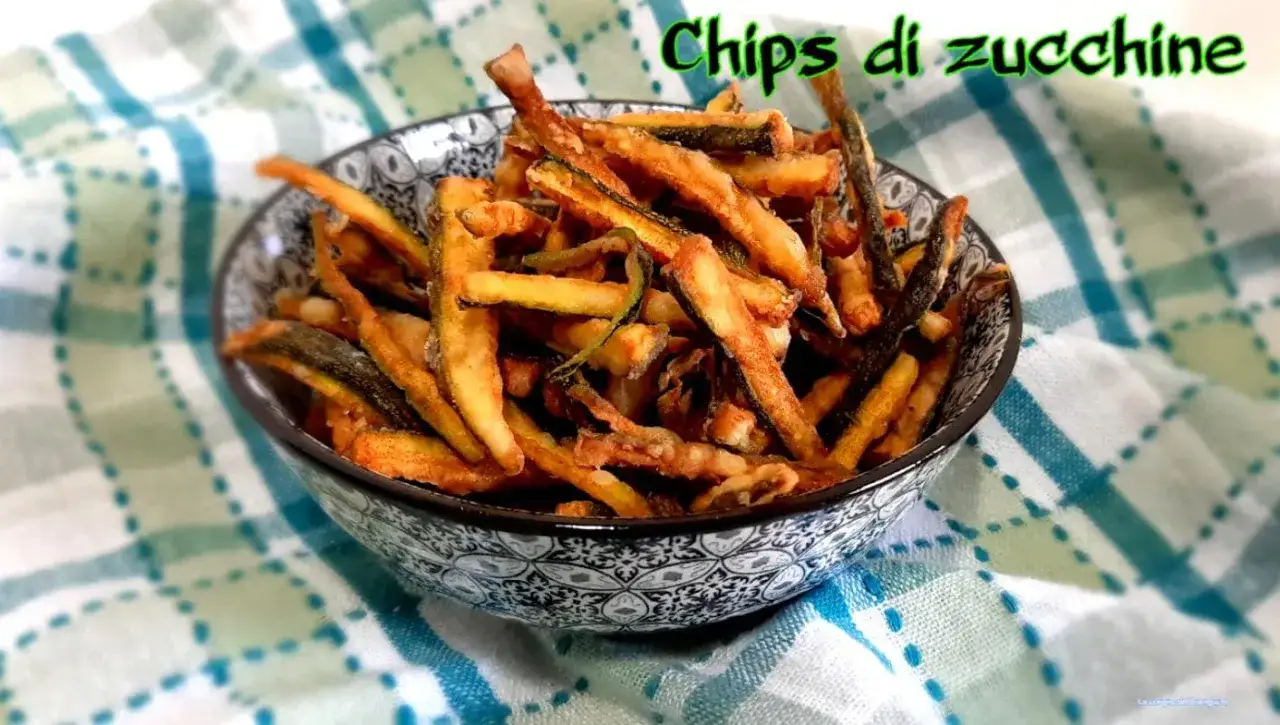 Croccanti chips di zucchine dorate, servite in una ciotola decorata su un tovagliolo a quadretti.