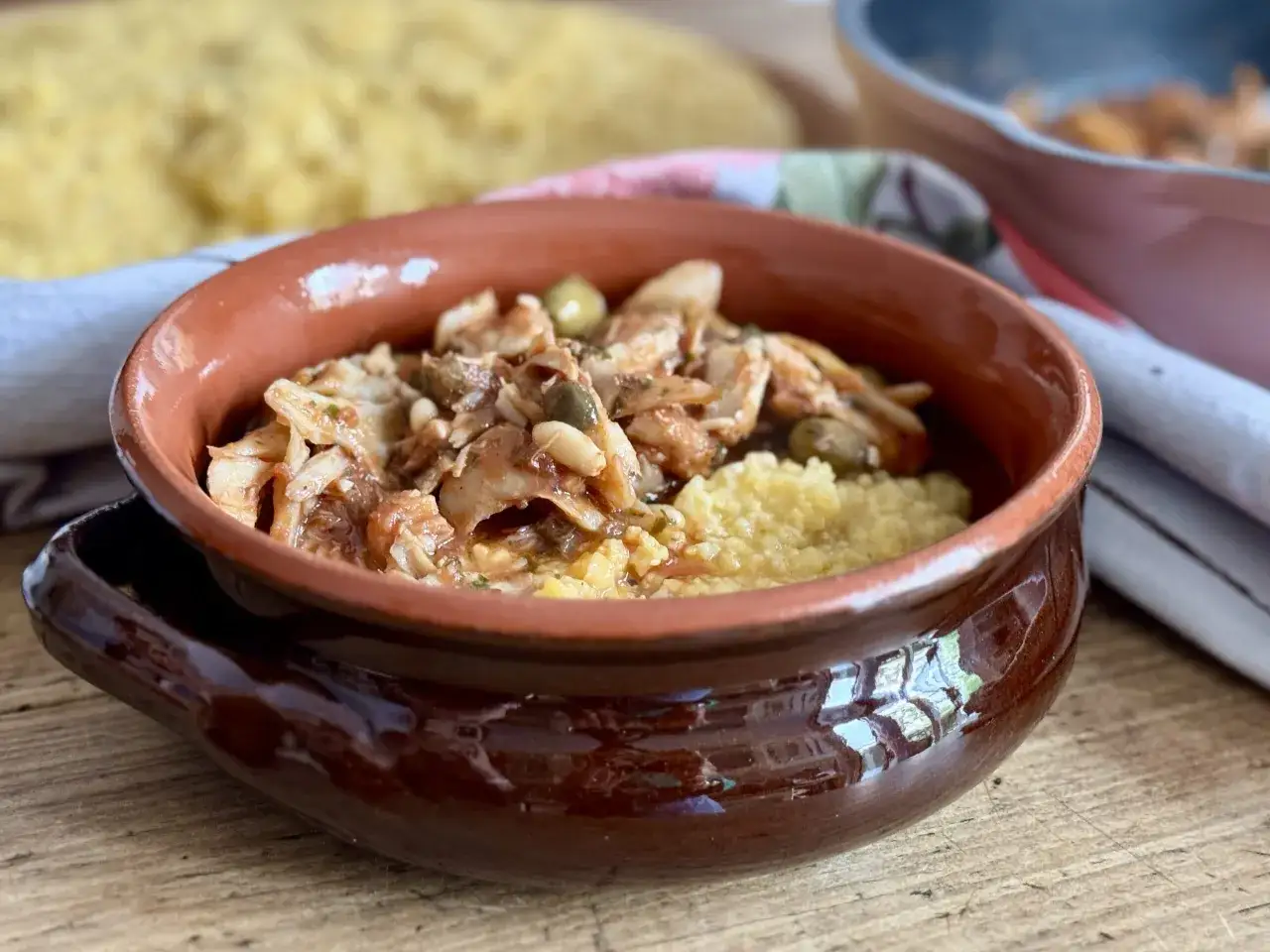 Piatto di baccal&agrave; alla vicentina servito in una ciotola di terracotta con polenta gialla.