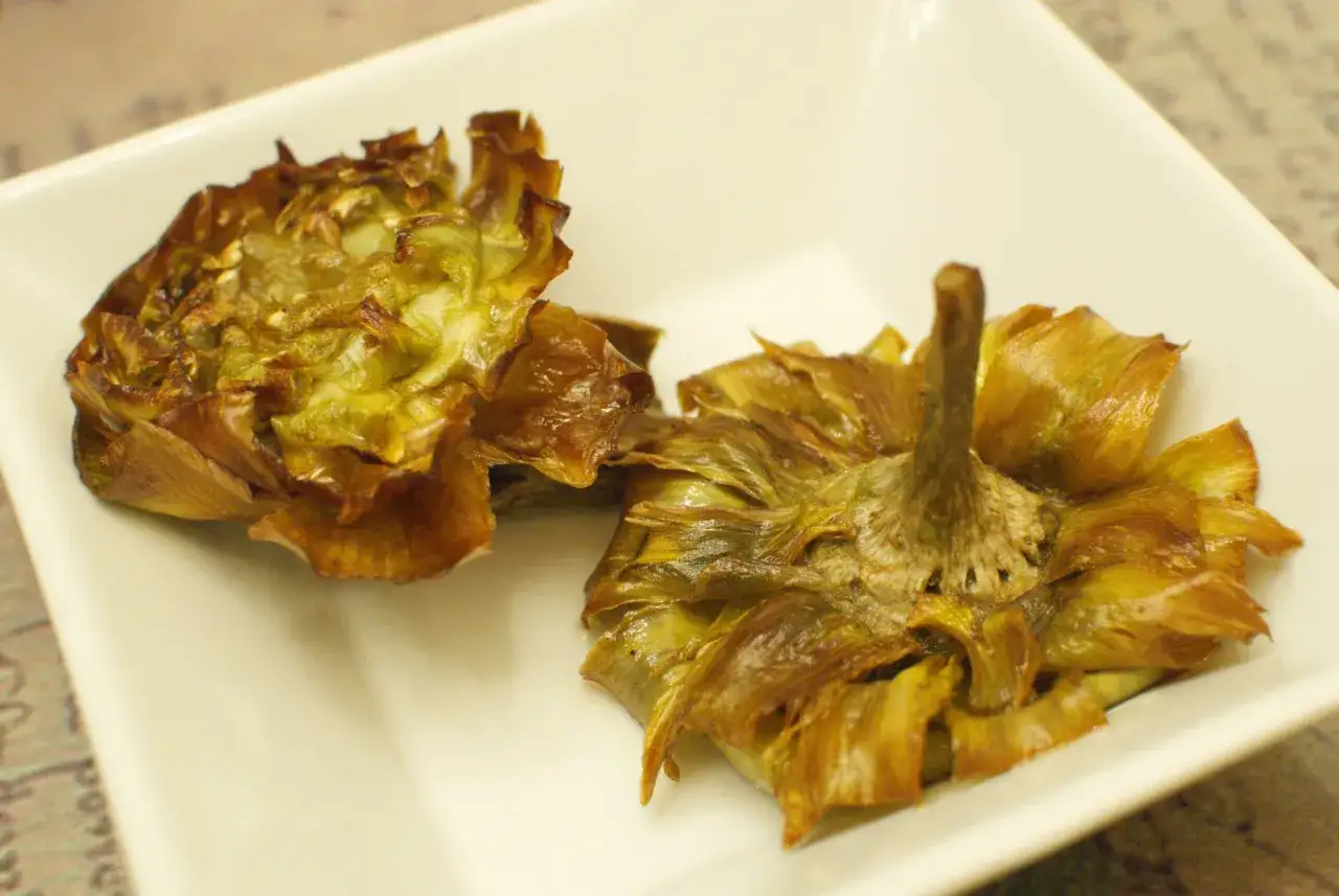 Due carciofi alla giudia dorati e croccanti, pronti per essere gustati in un piatto bianco.