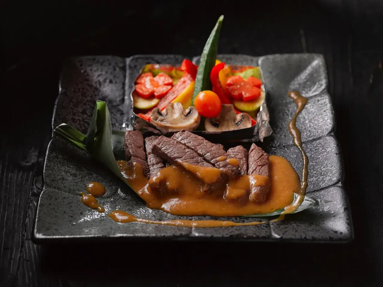 Straccetti di manzo succulenti su un piatto scuro, accompagnati da verdure miste e una salsa cremosa.