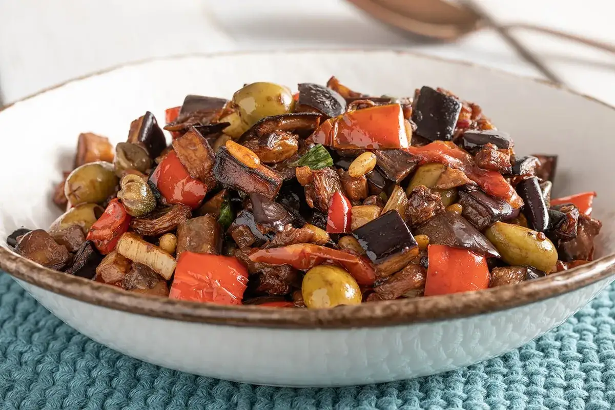 Caponata siciliana ricetta della nonna: melanzane, peperoni, olive e capperi in un piatto rustico, un sapore autentico.