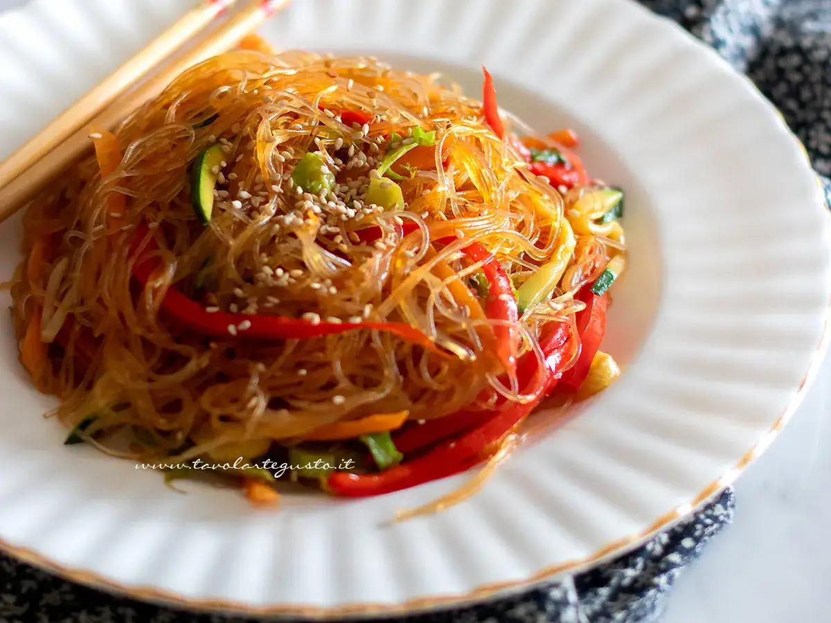 Deliziosi spaghetti di soia con verdure colorate, peperoni rossi, zucchine e carote, guarniti con semi di sesamo.