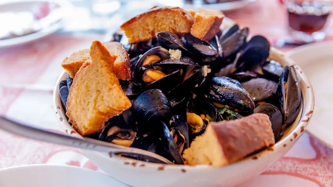 Un invitante piatto di zuppa di cozze, ricco di molluschi scuri e profumati, guarnito con crostini dorati.