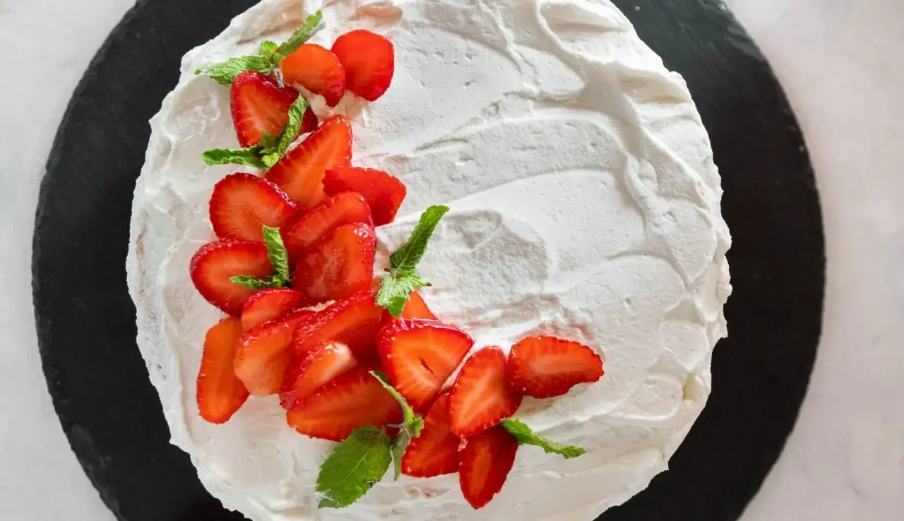 Deliziosa torta panna e fragole, con fragole fresche affettate e foglie di menta, su una base scura.